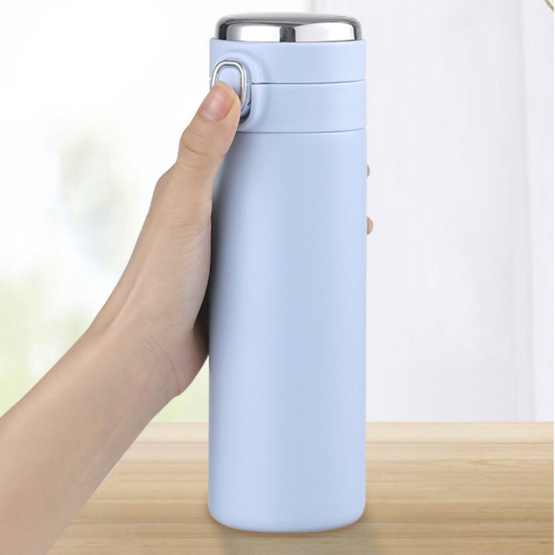 Light blue thermos held by a hand on a wooden surface with a white background
