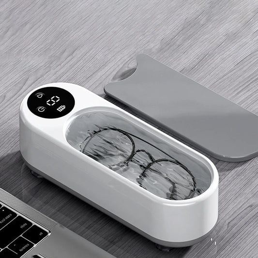White ultrasonic device with a digital display and glasses inside, on a wooden surface.
