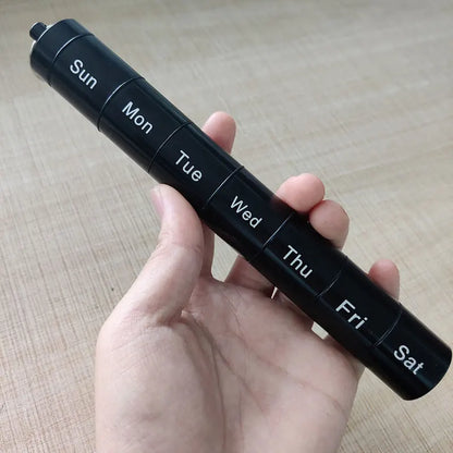 Black travel pill organizer with days of the week labels held in a hand on a wooden surface